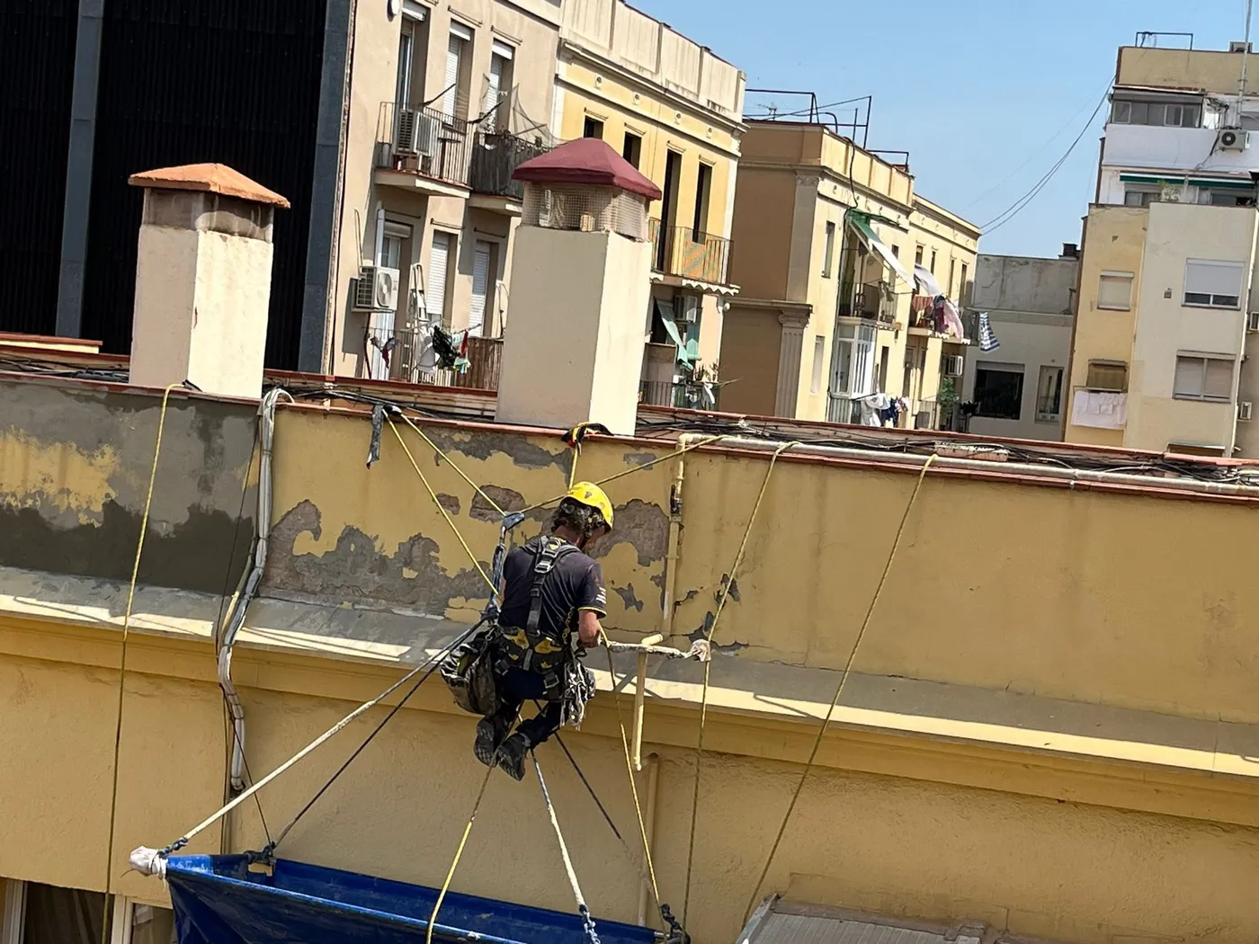 Operarios trabajando con cuerdas en la fachada de un edificio de viviendas del área de Barcelona