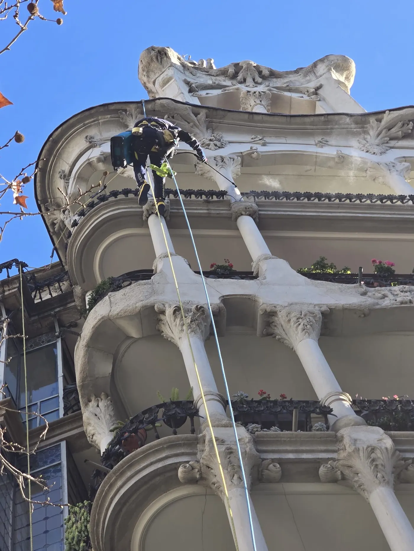 Técnico rehabilitando la cornisa de una fachada modernista con acceso por cuerdas