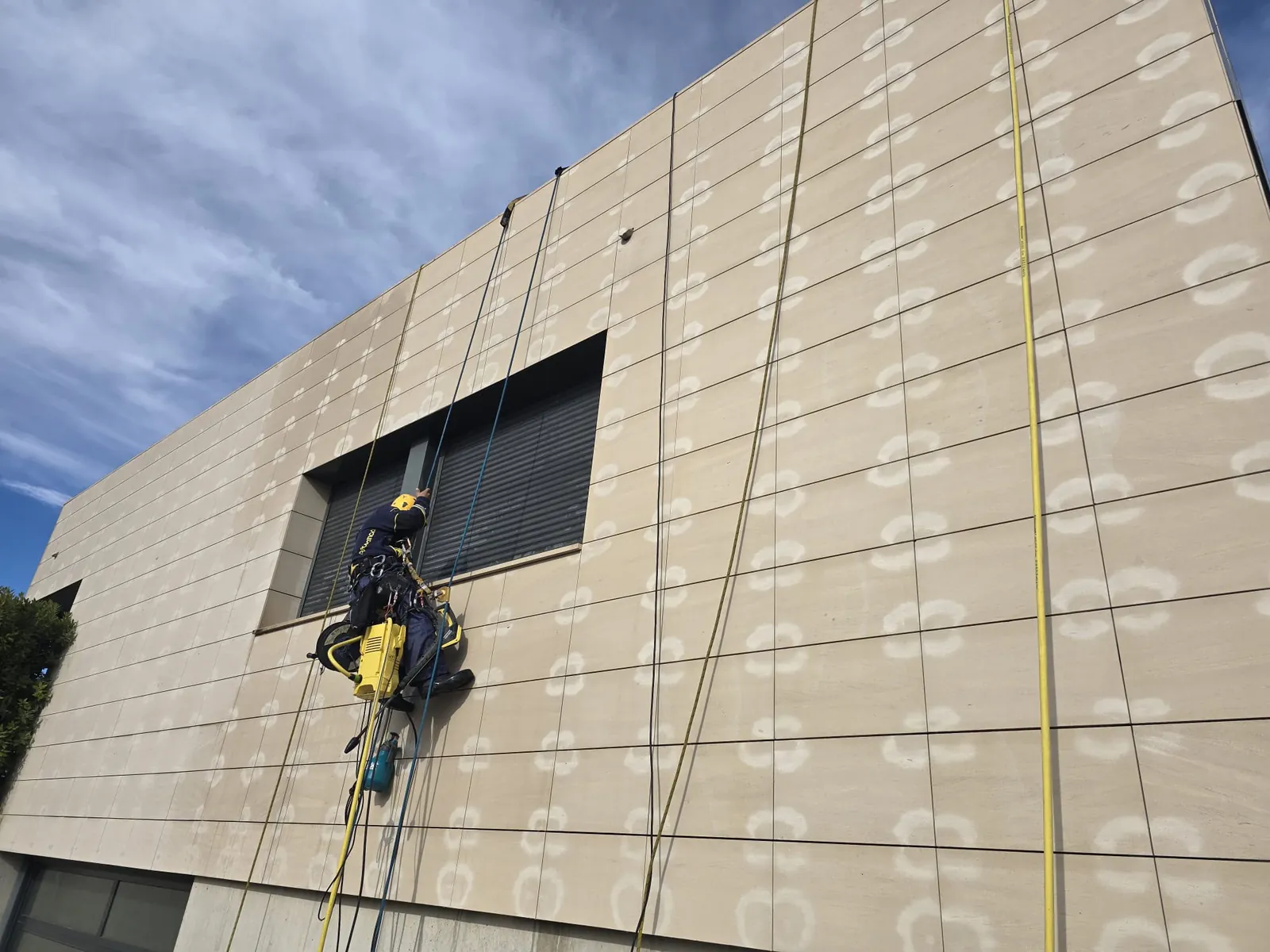 Técnico de trabajos verticales suspendido en la fachada de un edificio moderno